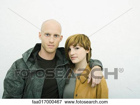 Stock Photo - Young adult couple looking at camera, man with arm around woman, portrait. Fotosearch