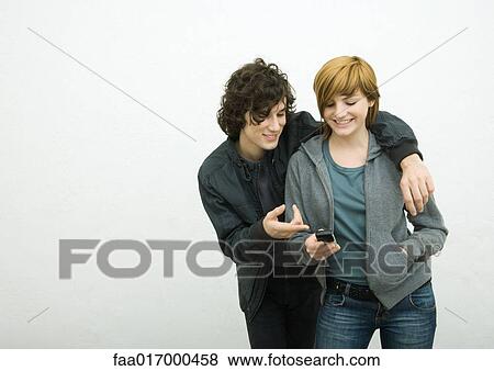 Young adult couple, man with arm around woman, woman holding cell phone View Large Photo Image Stock Photo - Young adult couple, man with arm around woman, woman holding cell phone. Fotosearch