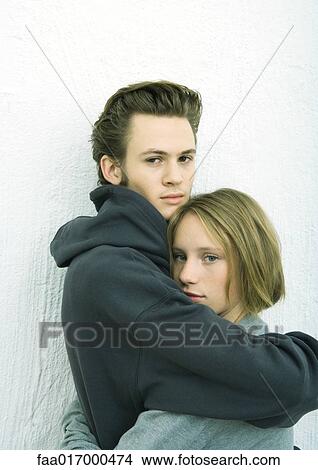 Picture - Young couple embracing, looking at camera, white background. Fotosearch