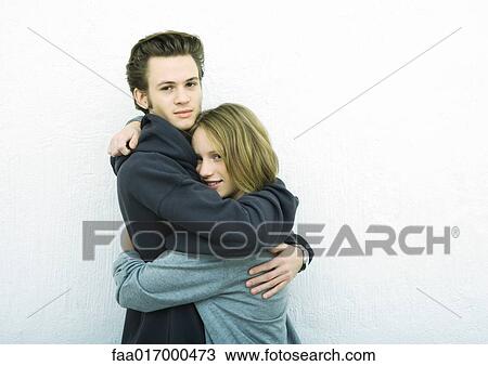 Stock Image - Young couple embracing, looking at camera, white background. Fotosearch