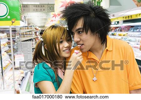 Young couple in grocery store, woman feeding man candy View Large Photo Image Stock Image - Young couple in grocery store, woman feeding man candy. Fotosearch