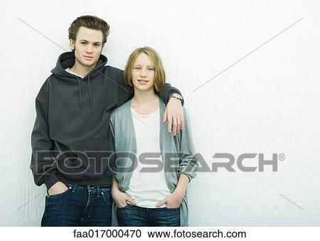 Stock Image - Young couple leaning against wall, looking at camera, portrait. Fotosearch