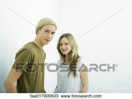 Stock Image - Young couple looking at camera, portrait, white background. Fotosearch