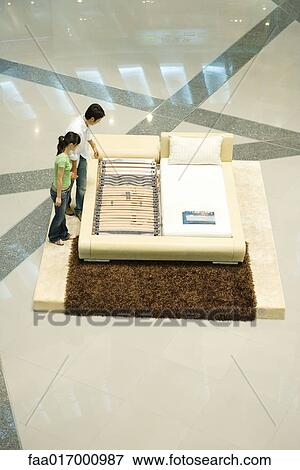 Stock Photo - Young couple looking at mattress display, high angle view. Fotosearch