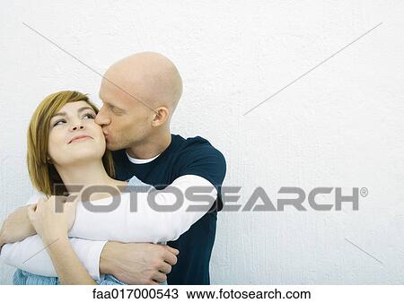Stock Image - Young couple, man kissing woman's cheek woman from behind. Fotosearch