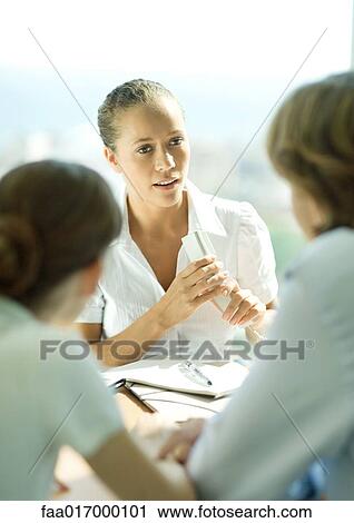 Stock Image - Young couple sitting across table from young female professional holding phone. Fotosearch