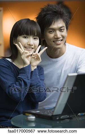 Young couple using laptop, woman making "v" signs with fingers View Large Photo Image Stock Photo - Young couple using laptop, woman making "v" signs with fingers. Fotosearch