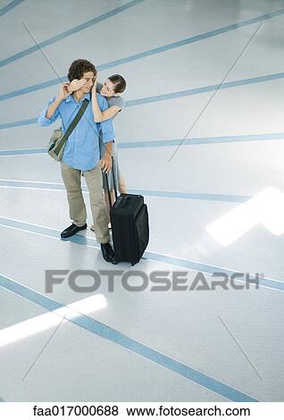 Stock Photo - Young couple, woman standing behind boyfriend who is looking over shoulder, full length. Fotosearch