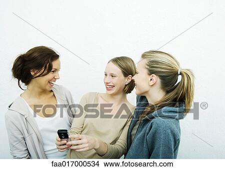 Young female friends looking at cell phone together View Large Photo Image Picture - Young female friends looking at cell phone together. Fotosearch