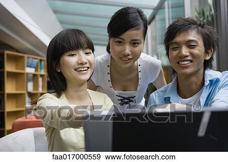 Young friends looking at laptop together View Large Photo Image Stock Photo - Young friends looking at laptop together. Fotosearch