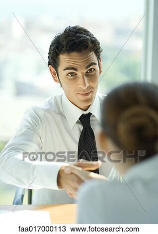 Young male professional shaking hands across table View Large Photo Image Stock Image - Young male professional shaking hands across table. Fotosearch