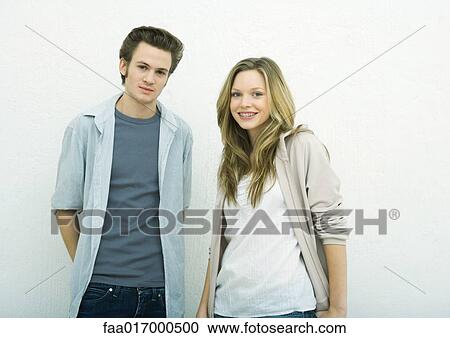 Stock Image - Young man and teenage girl standing side by side, looking at camera, portrait. Fotosearch
