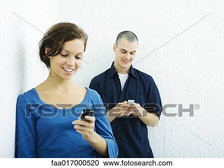 Stock Image - Young man and young woman using cell phones. Fotosearch