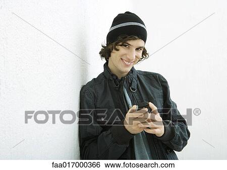 Young man holding cell phone, smiling at camera, white background View Large Photo Image Stock Photograph - Young man holding cell phone, smiling at camera, white background. Fotosearch