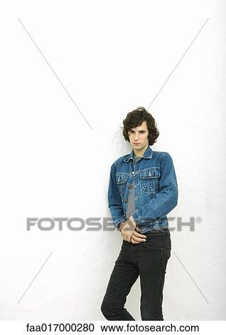 Stock Image - Young man leaning against wall, portrait. Fotosearch