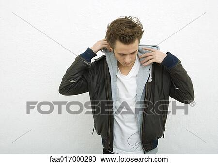 Stock Image - Young man putting on hood, portrait. Fotosearch