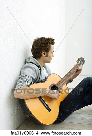 Young man sitting on floor, playing guitar View Large Photo Image Picture - Young man sitting on floor, playing guitar. Fotosearch