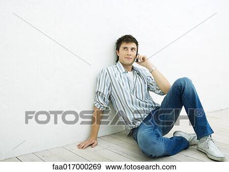 Stock Photo - Young man sitting on floor, using cell phone. Fotosearch