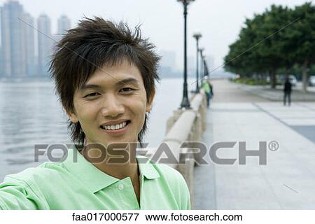 Young man standing by riverside View Large Photo Image Stock Photo - Young man standing by riverside. Fotosearch