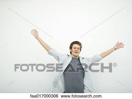 Young man standing with arms up, smiling, portrait View Large Photo Image Stock Photograph - Young man standing with arms up, smiling, portrait. Fotosearch
