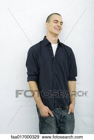 Stock Photo - Young man standing with hands in pockets, eyes closed, portrait. Fotosearch