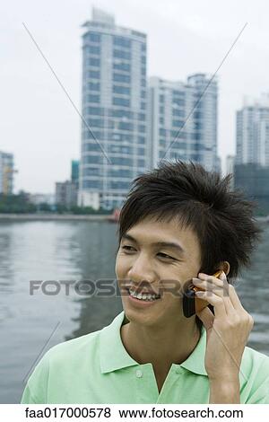 Young man using cell phone by river View Large Photo Image Stock Photo - Young man using cell phone by river. Fotosearch