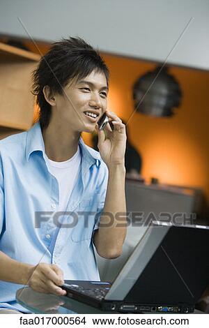 Picture - Young man using laptop and cell phone. Fotosearch