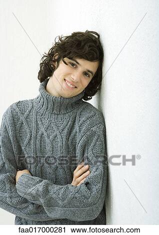 Stock Image - Young man wearing sweater, leaning against wall, portrait. Fotosearch