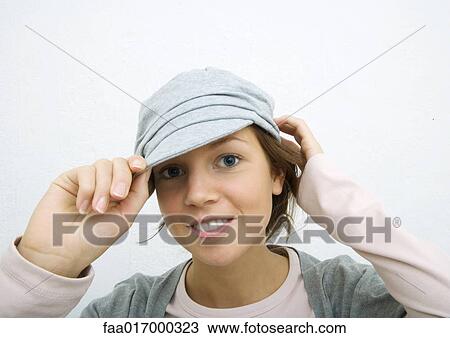 Stock Image - Young woman adjusting cap, portrait. Fotosearch