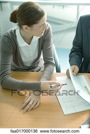 Stock Photograph - Young woman holding pen poised over documents. Fotosearch