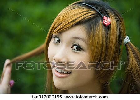 Young woman holding pigtail and smiling at camera, close-up, portrait View Large Photo Image Stock Photography - Young woman holding pigtail and smiling at camera, close-up, portrait. Fotosearch