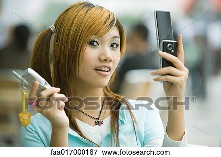 Young woman holding two cell phones, looking at camera View Large Photo Image Stock Photo - Young woman holding two cell phones, looking at camera. Fotosearch