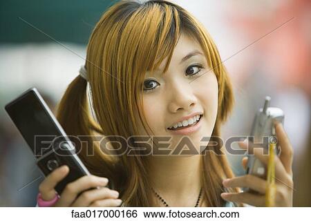 Young woman holding two cell phones, looking at camera View Large Photo Image Stock Photograph - Young woman holding two cell phones, looking at camera. Fotosearch