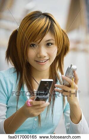 Stock Photography - Young woman holding two cell phones, looking at camera. Fotosearch