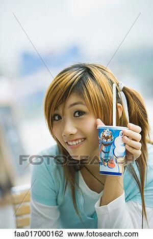 Young woman holding up fast food drink, smiling at camera View Large Photo Image Stock Image - Young woman holding up fast food drink, smiling at camera. Fotosearch