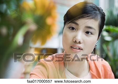 Young woman listening to earphones and looking at flower View Large Photo Image Stock Photo - Young woman listening to earphones and looking at flower. Fotosearch