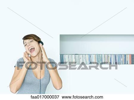 Stock Photo - Young woman listening to headphones and singing, next to row of CDs, eyes closed. Fotosearch
