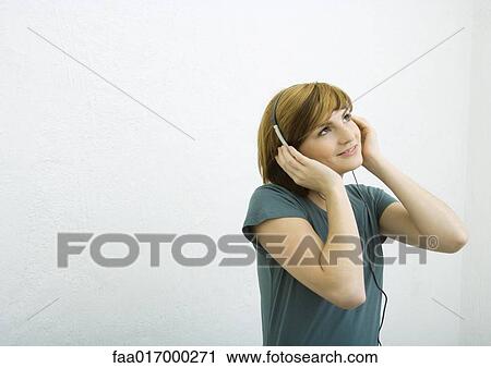 Young woman listening to headphones, smiling and looking up View Large Photo Image Stock Image - Young woman listening to headphones, smiling and looking up. Fotosearch
