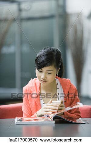 Stock Image - Young woman looking through magazine. Fotosearch