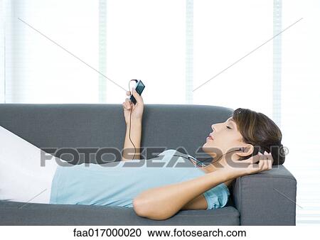 Stock Image - Young woman lying on couch, listening to MP3 player. Fotosearch