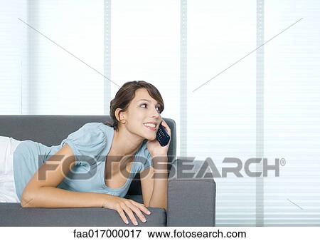 Stock Photo - Young woman lying on couch, using cell phone. Fotosearch