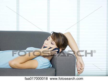 Young woman lying on couch, using cell phone View Large Photo Image Stock Photo - Young woman lying on couch, using cell phone. Fotosearch