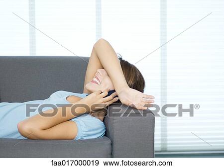 Young woman lying on couch, using cell phone, arm over eyes View Large Photo Image Stock Photo - Young woman lying on couch, using cell phone, arm over eyes. Fotosearch