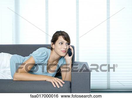 Stock Photograph - Young woman lying on couch, using cell phone. Fotosearch