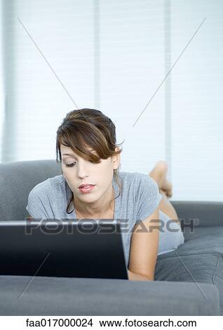 Young woman lying on couch, using laptop View Large Photo Image Picture - Young woman lying on couch, using laptop. Fotosearch
