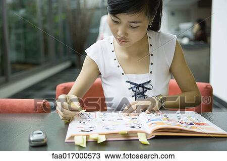Stock Image - Young woman marking book with adhesive notes. Fotosearch