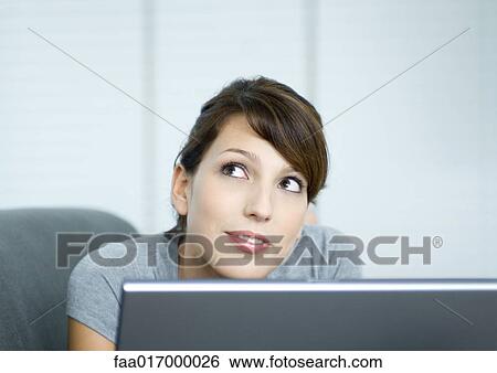 Stock Photograph - Young woman on couch, using laptop. Fotosearch