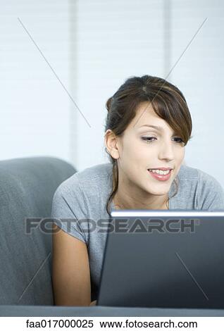 Young woman on couch, using laptop View Large Photo Image Stock Photography - Young woman on couch, using laptop. Fotosearch