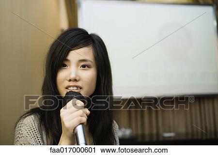 Stock Image - Young woman singing karaoke. Fotosearch