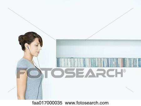 Young woman standing, listening to earphones, next to row of CDs, eyes closed View Large Photo Image Stock Photography - Young woman standing, listening to earphones, next to row of CDs, eyes closed. Fotosearch